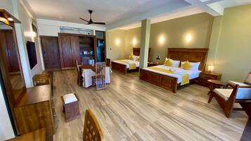 A hotel room with a wooden floor, a bed with a headboard, a desk, a chair, and a wardrobe.
