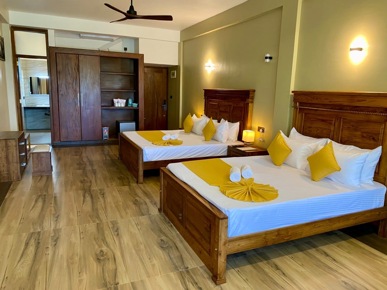 A hotel room with two beds, wooden flooring, a wardrobe, and a desk.