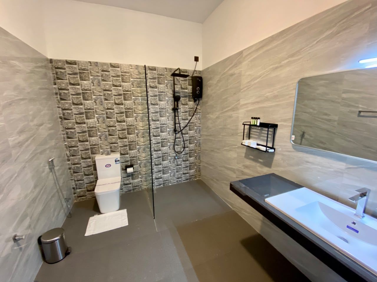 A modern bathroom with a stone wall, a glass shower enclosure, a white toilet, and a large mirror.