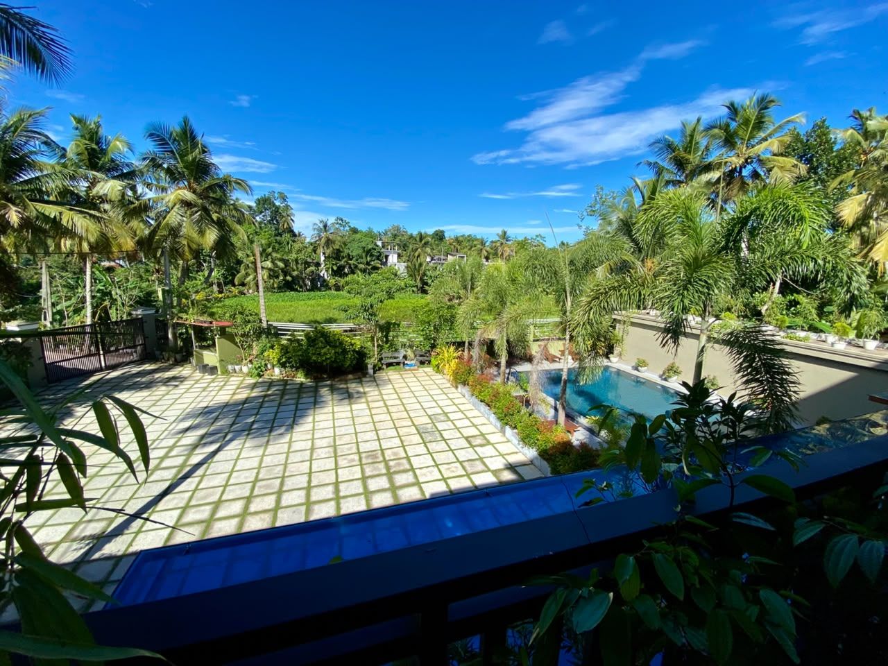 A pool area with tiled flooring, surrounded by lush greenery and palm trees.