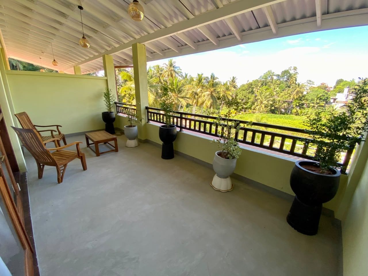 A covered balcony with seating, potted plants, and a view of greenery.