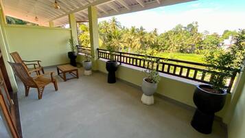 A covered balcony with seating, potted plants, and a view of greenery.