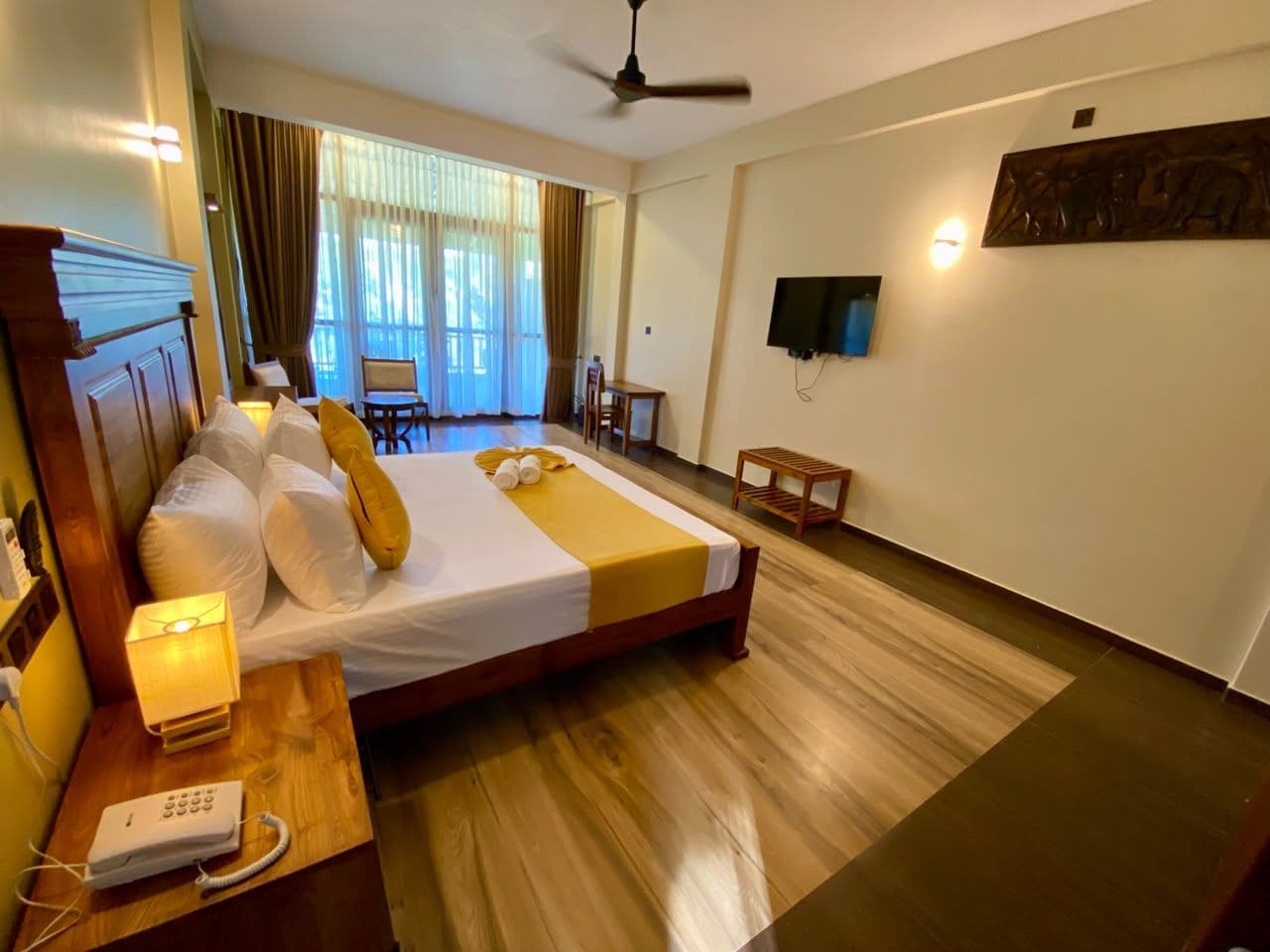 A hotel room with a bed, bedside table, lamp, and a television mounted on the wall.
