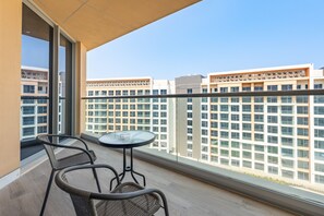 A balcony with a round table and two chairs, overlooking a cityscape with modern buildings. - Seaside 2BR & AsstRm w/ Gulf of Oman Views, Minutes from Khorfakkan Waterfalls (Khor Fakkan)