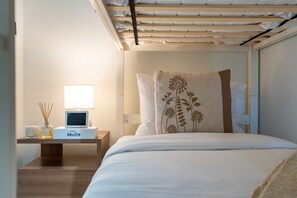 Een hotelkamer met een bed, een nachtkastje met een lamp, een klein tafeltje met een fles en een doos, en een aan de muur bevestigde televisie.