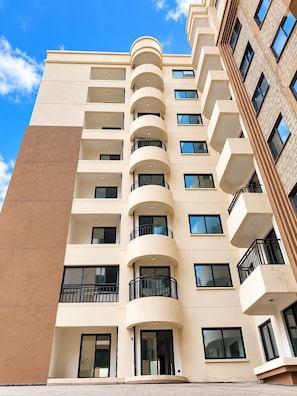 A multi-story hotel with a beige facade, multiple balconies, and a clear sky in the background. - 

Nova Stays | Cozy Studio Near JKIA & SGR (Nairobi)