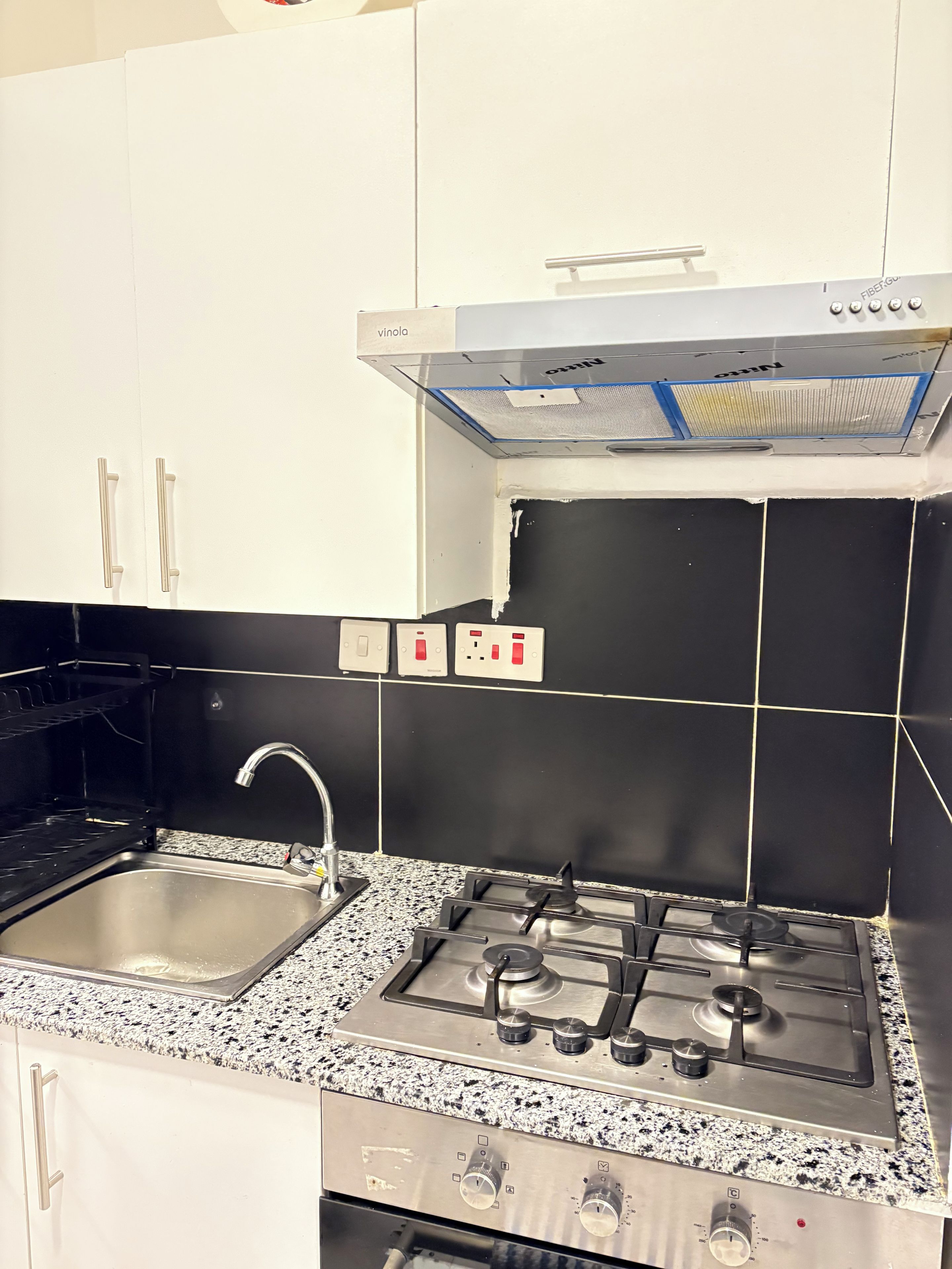 A kitchen with white cabinets, a stainless steel sink, a gas stove, and a black tiled backsplash.