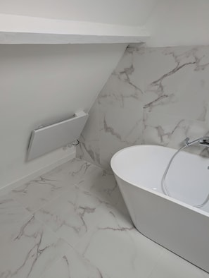 Un baño moderno con una bañera independiente, suelo de mármol y un radiador blanco.
