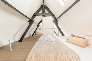 Un dormitorio con techo inclinado, una cama con manta color beige, almohada blanca y almohada marrón.