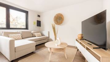 A modern living room with a sofa, a round coffee table, a TV, and a decorative wall piece.