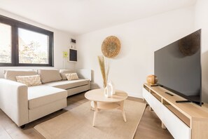 Una sala de estar moderna con un sofá, una mesa redonda de centro, un televisor y un adorno en la pared.