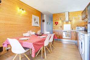 A dining area with a table set for four, wooden walls, and a kitchen with modern appliances. - Le Cocon du Capcir - Avec Balcon (Les Angles)