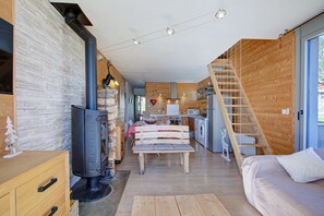 A modern interior with a central fireplace, wooden walls, a dining area, and a kitchen. - Le Cocon du Capcir - Avec Balcon (Les Angles)