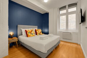 A bedroom with a bed, a nightstand, a lamp, a window with blinds, and a wall-mounted TV. - L'Orfèvre - A deux pas de la Place du Capitole (Toulouse)