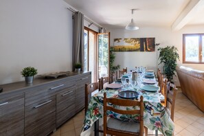 En matplats med ett bord dukat för fyra personer, trästolar, en bänk, ett skåp och en tavla på väggen.