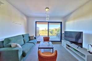 A modern living room with a sofa, a table, a TV, and a balcony with a view. - Les Jardins de Vignola - Proche du Port (Porto-Vecchio)