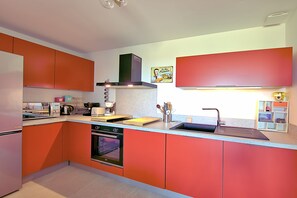 A modern kitchen with orange cabinetry, a built-in oven, and a stainless steel sink. - Les Jardins de Vignola - Proche du Port (Porto-Vecchio)