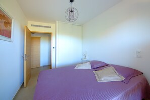 A bedroom with a bed, a door, a light fixture, and a wall-mounted thermostat. - Les Jardins de Vignola - Proche du Port (Porto-Vecchio)