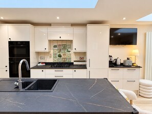 A modern kitchen with a central island, built-in oven, and a flat-screen TV above the counter. - Gore Park House - Victorian Charm & Modern Comfort (Eastbourne)