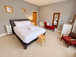Ein Schlafzimmer mit einem Bett, Nachttischen, einem roten Sessel, einem hölzernen Hocker, einem Spiegel und einer Heizung.