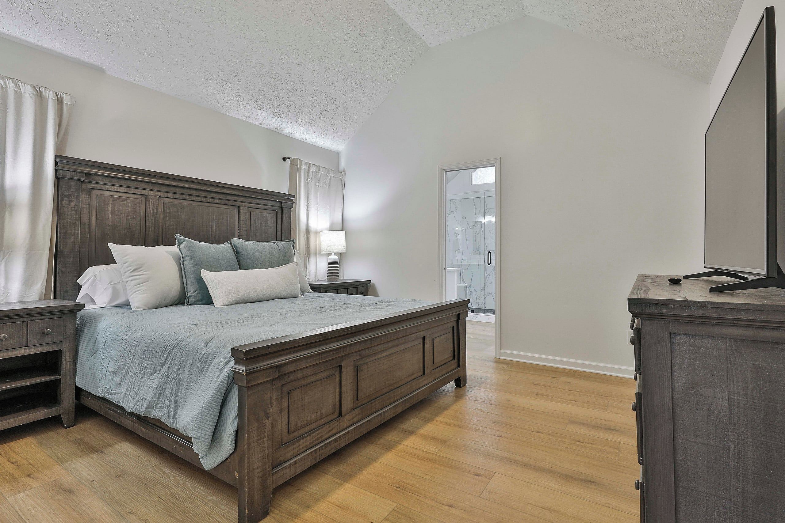 Une chambre à coucher avec un lit en bois, une table de chevet, une commode et un téléviseur.