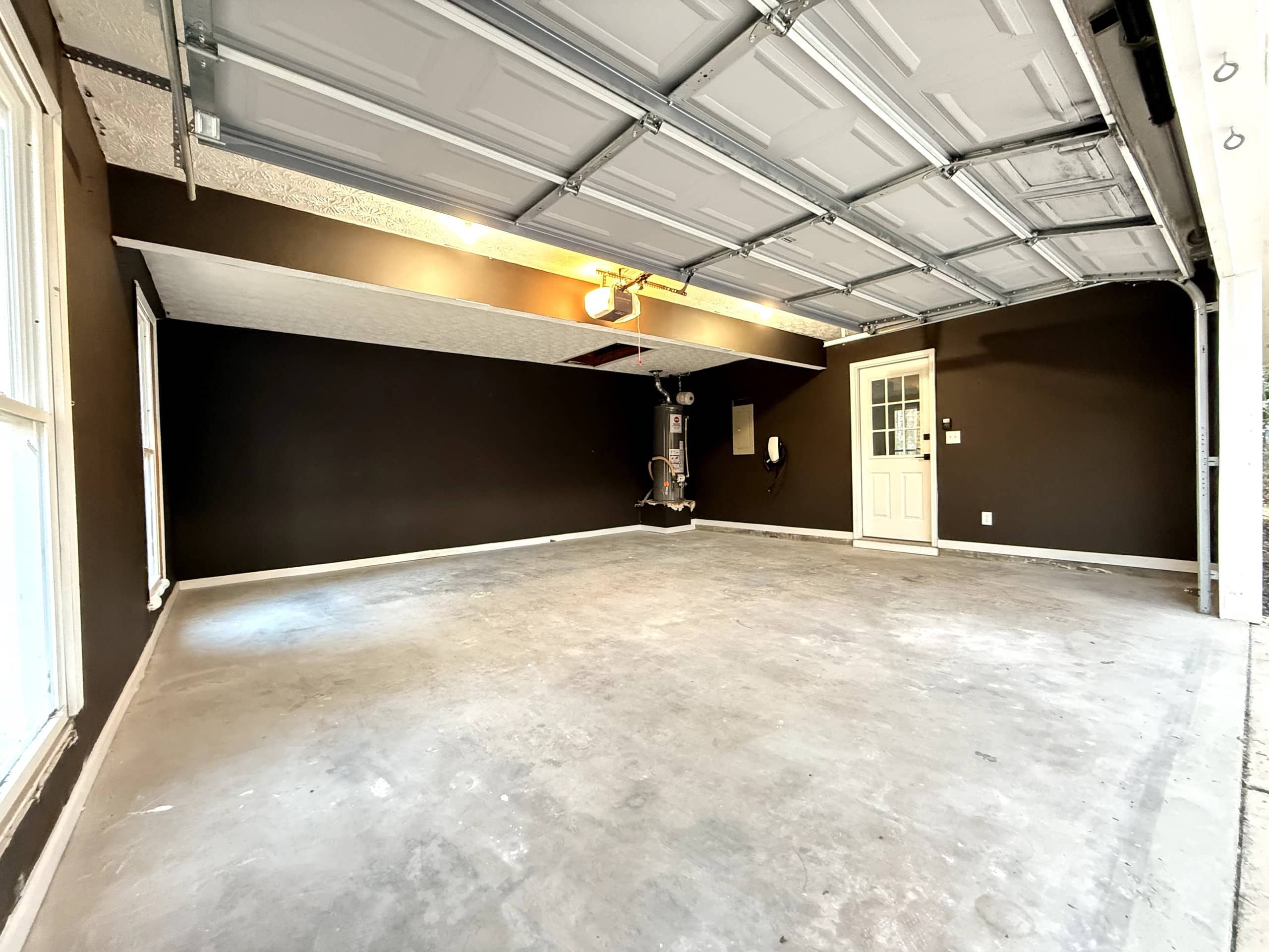 Un grand garage doté d’un sol en béton, d’une porte et d’un plafond où les conduits sont apparents.