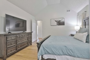 Une chambre à coucher avec un lit, une commode, une télévision et des œuvres d’art.