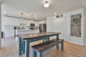 Une cuisine moderne avec des meubles blancs, des appareils en acier inoxydable et une table en bois de couleur turquoise, accompagnée d’un banc.