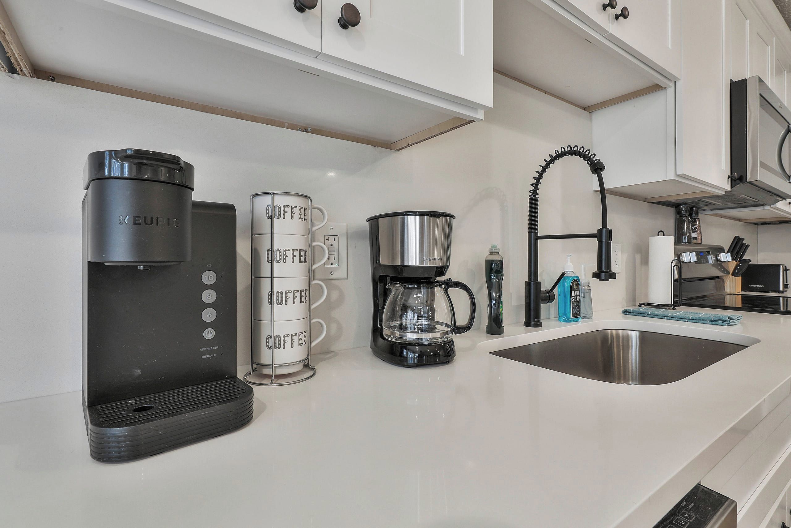 Une cuisine moderne équipée d’une machine à café, d’une balance, d’une bouilloire et d’un évier.