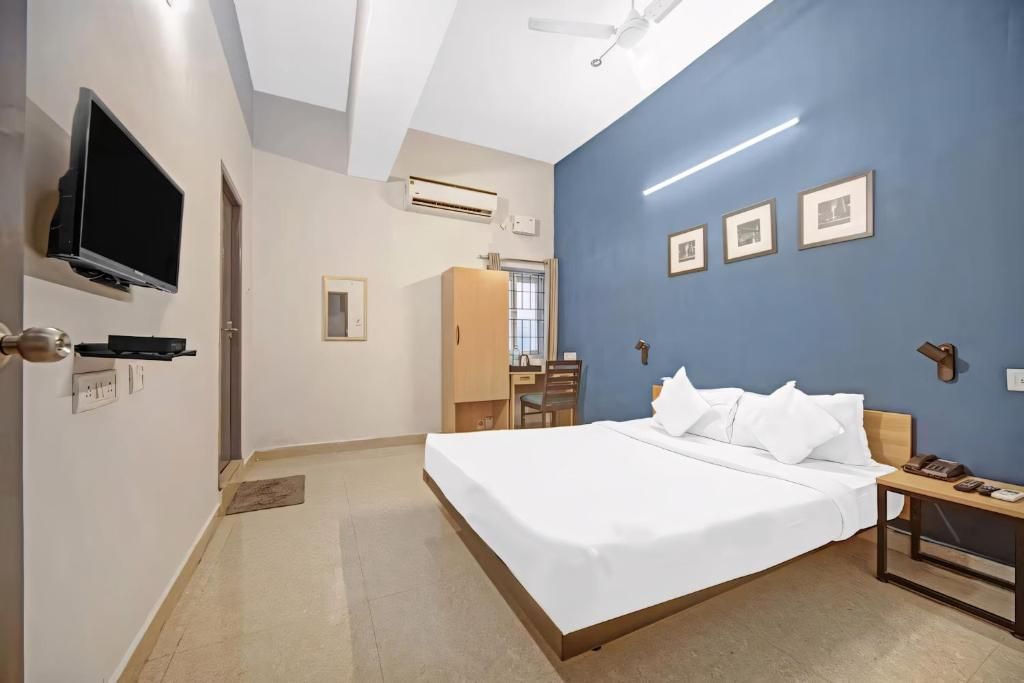 Ett hotellrum med en säng, ett skrivbord, en stol, en tv och en takfläkt.