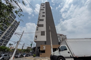 A tall, modern building with a prominent vertical structure and a ground-level entrance. - Brooklyn by Bhomy (São Paulo)