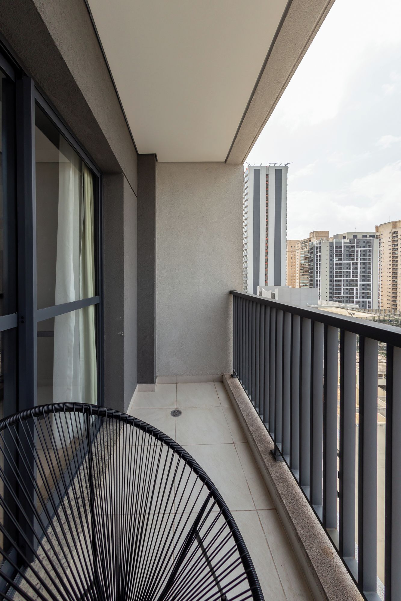 A balcony with a metal railing, a chair, and a view of surrounding buildings.