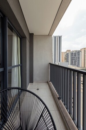 Un balcon doté d’une rambarde en métal, d’une chaise et offrant une vue sur les bâtiments environnants.