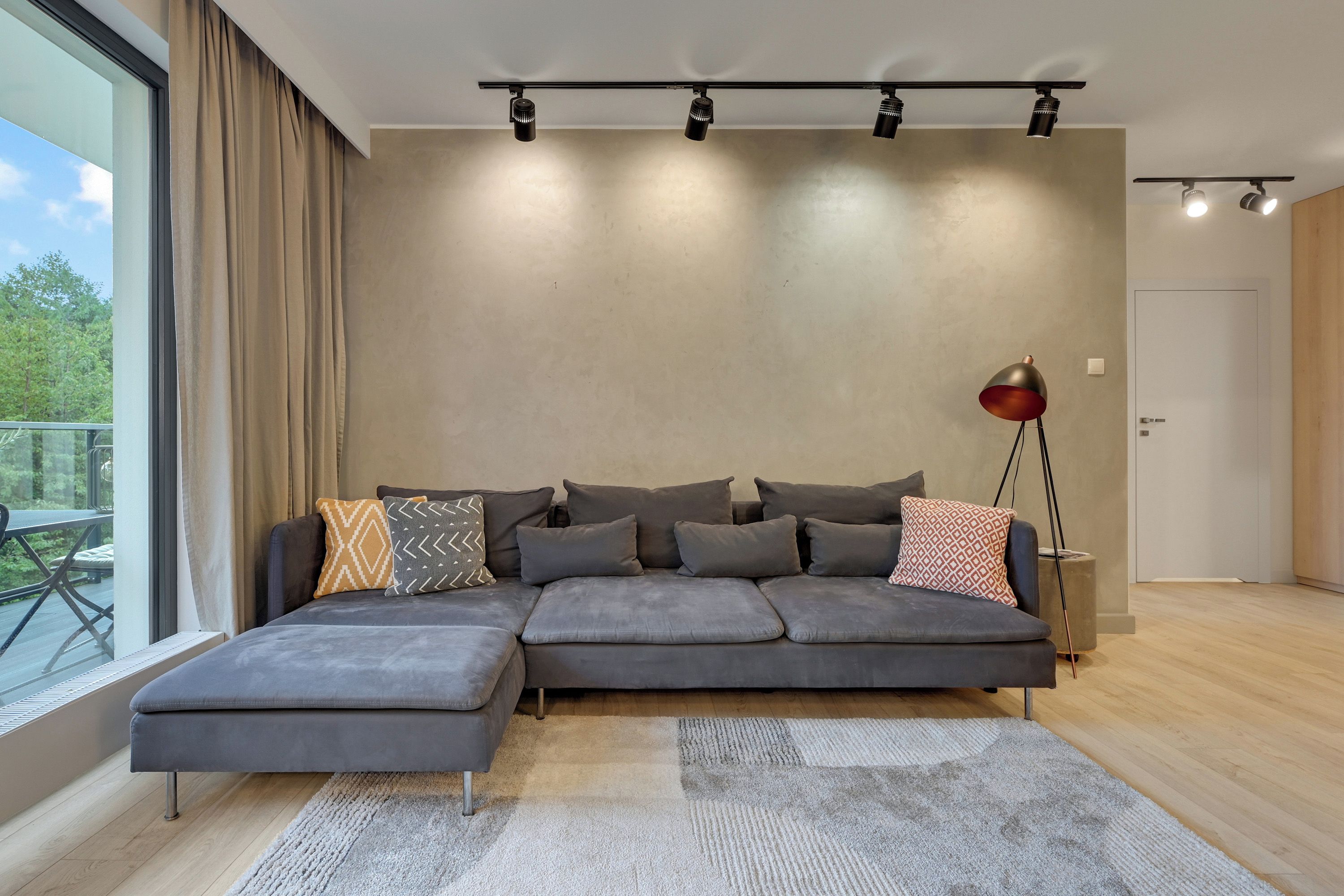 Una sala de estar moderna con un sofá modular, una lámpara de pie y un ventanal con cortinas.