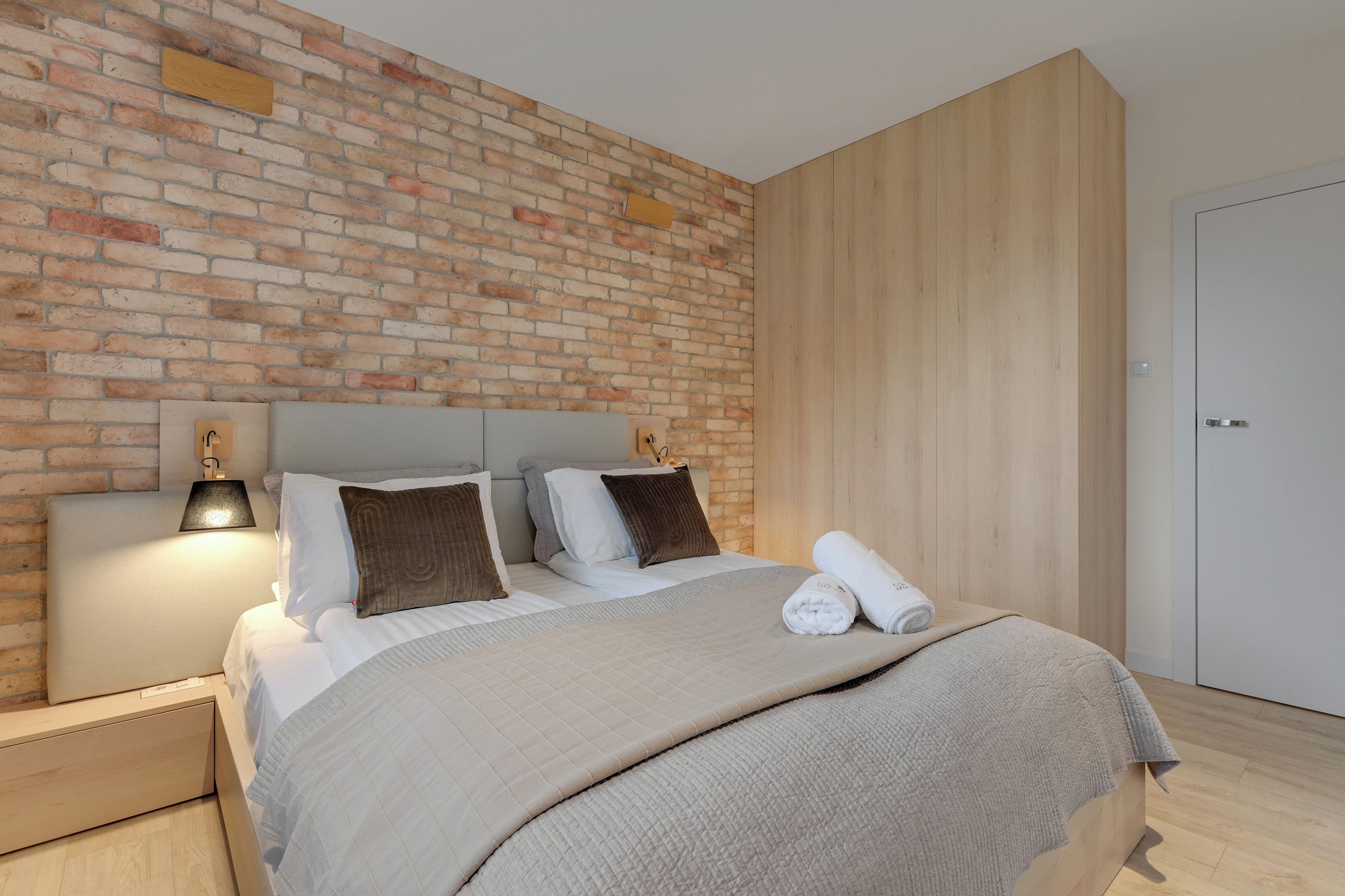 Un dormitorio moderno con pared de ladrillo, cabecero de madera y puerta blanca.