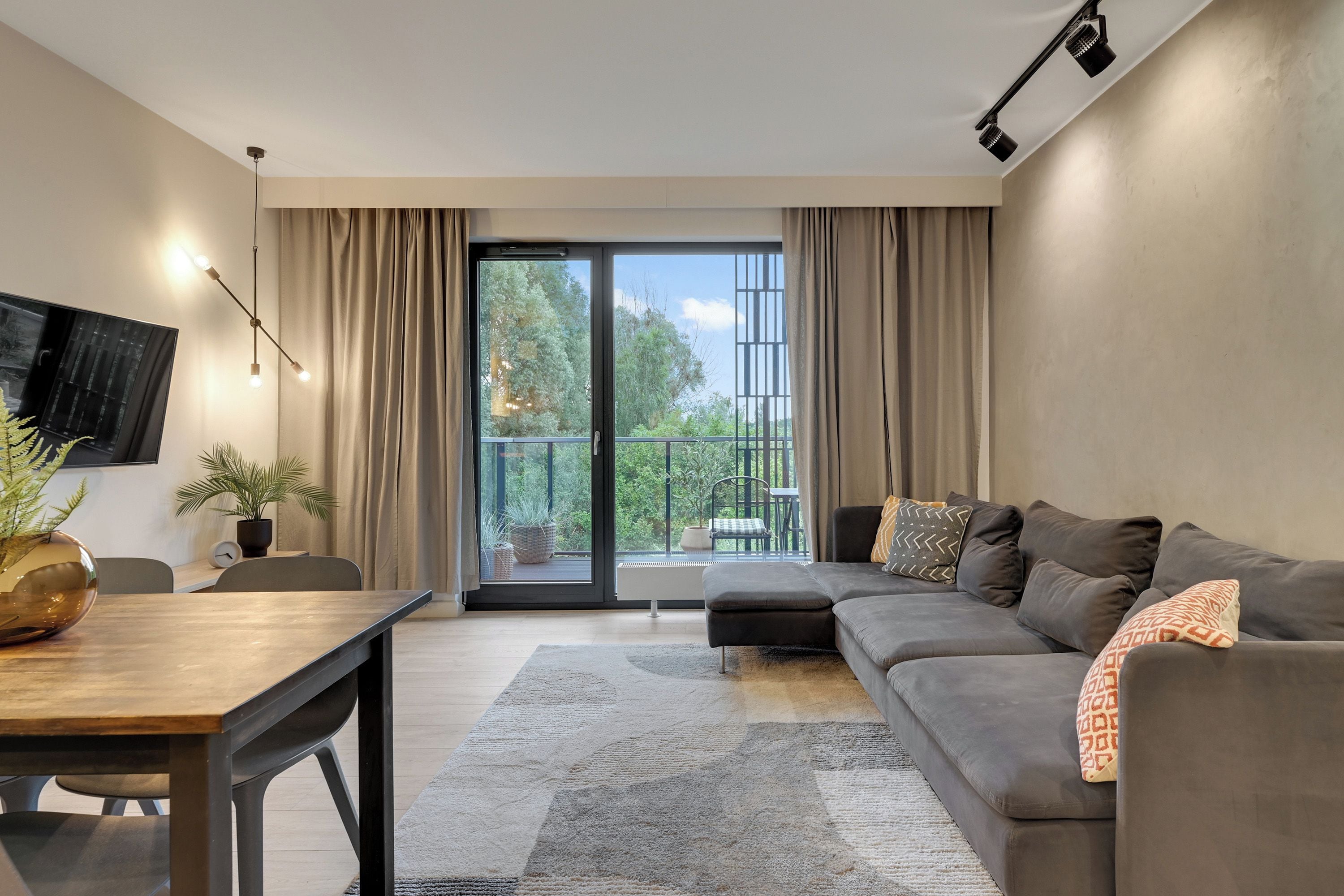 A modern living room with a sofa, a dining table, and a TV mounted on the wall.