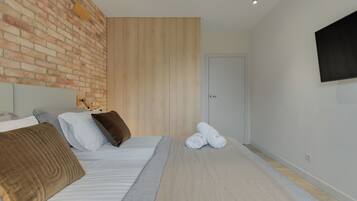 Un dormitorio moderno con pared de ladrillo, paneles de madera, una cama con almohadas, un televisor de pantalla plana y una puerta.