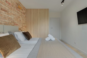 Un dormitorio moderno con pared de ladrillo, paneles de madera, una cama con almohadas, un televisor de pantalla plana y una puerta.