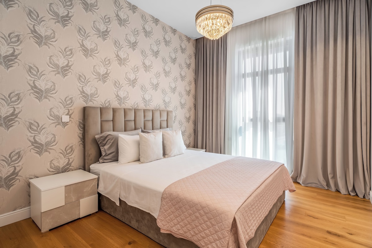 A bedroom with a bed, bedside tables, a chandelier, and a window with curtains.