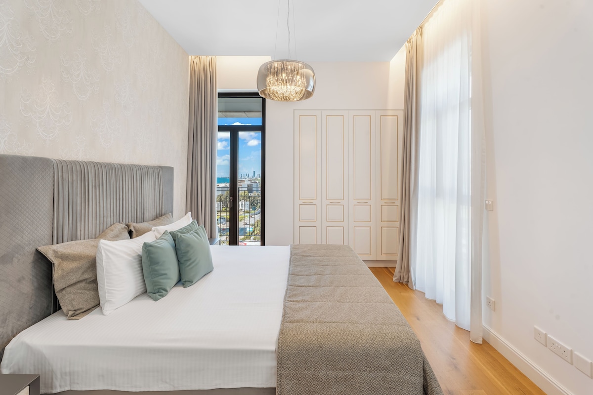 A modern bedroom with a large bed, a view of the city through a balcony, and a chandelier.