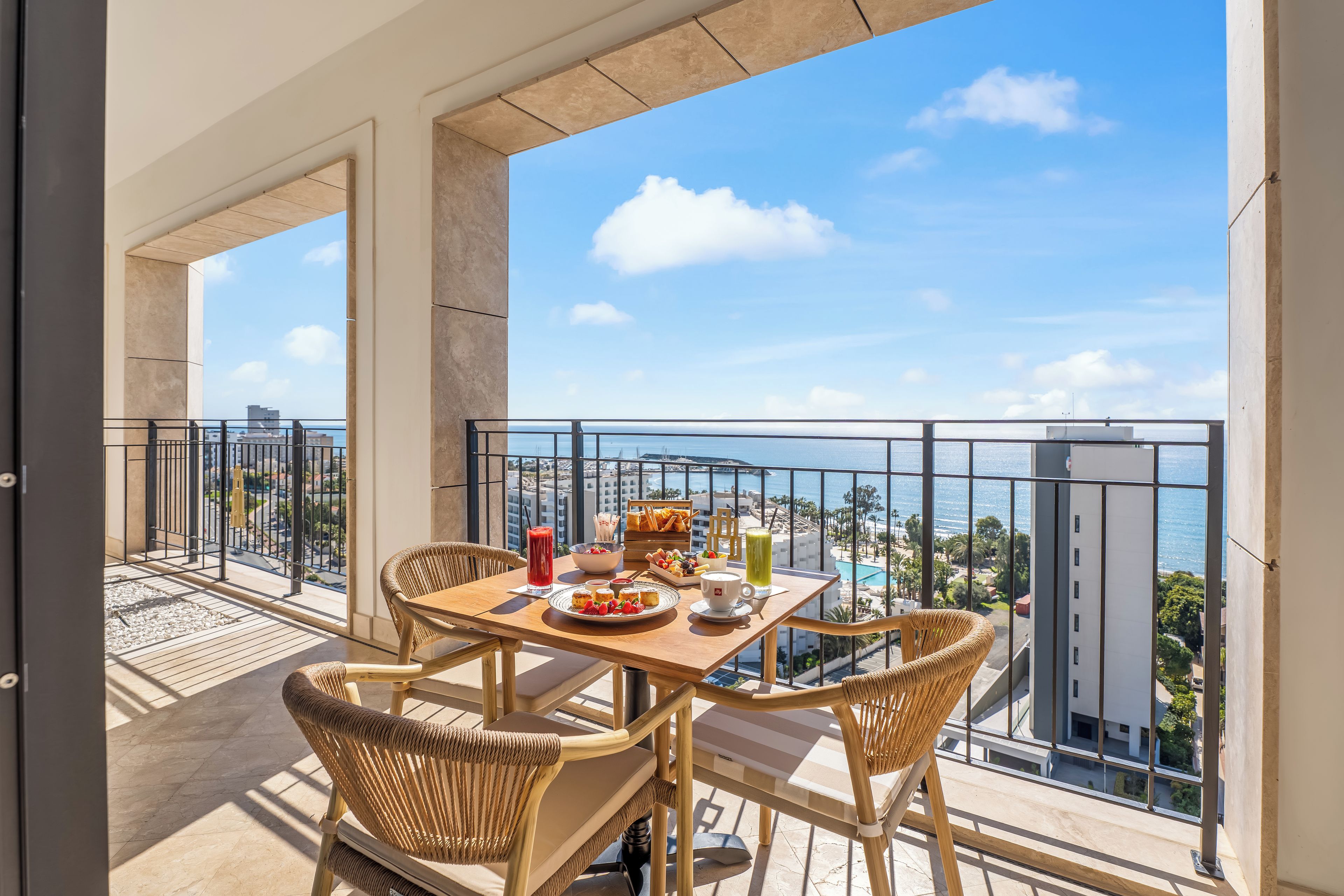A balcony with a table set for breakfast, overlooking a pool and cityscape.
