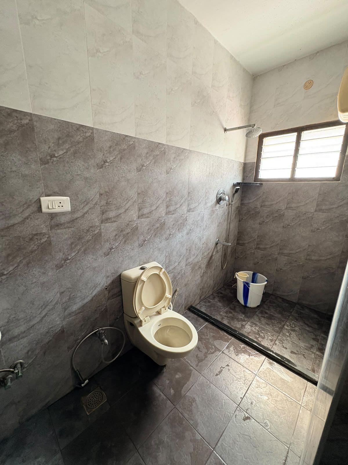 Een badkamer met toilet, douche en een raam.