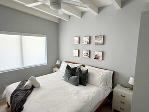 Ein Schlafzimmer mit einem Bett, Nachttischen, einem Deckenventilator und Kunstwerken an der Wand.