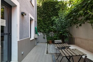 Un pequeño patio exterior con un banco y una mesa, rodeado por un muro cubierto de plantas trepadoras.