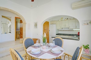 A dining area with a round table set for four, flanked by two chairs, and a kitchen visible through an archway. - Casa La Calma – Holiday Home with Private Pool (el Cim del Sol)