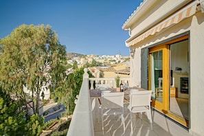 A balcony with a table set for dining, overlooking a residential area with houses and a hill in the distance. - Casa La Calma – Holiday Home with Private Pool (el Cim del Sol)