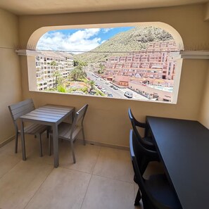 A balcony with a view of a residential area, a table, and two chairs. - 2 Bed Duplex in Castle Harbour C207' with Shared Pool, Wi-Fi and Air Conditioning (Los Cristianos)