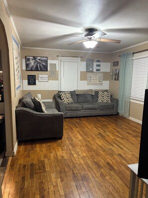 A living room with a ceiling fan, two grey sofas, wooden flooring, and various wall decorations.
