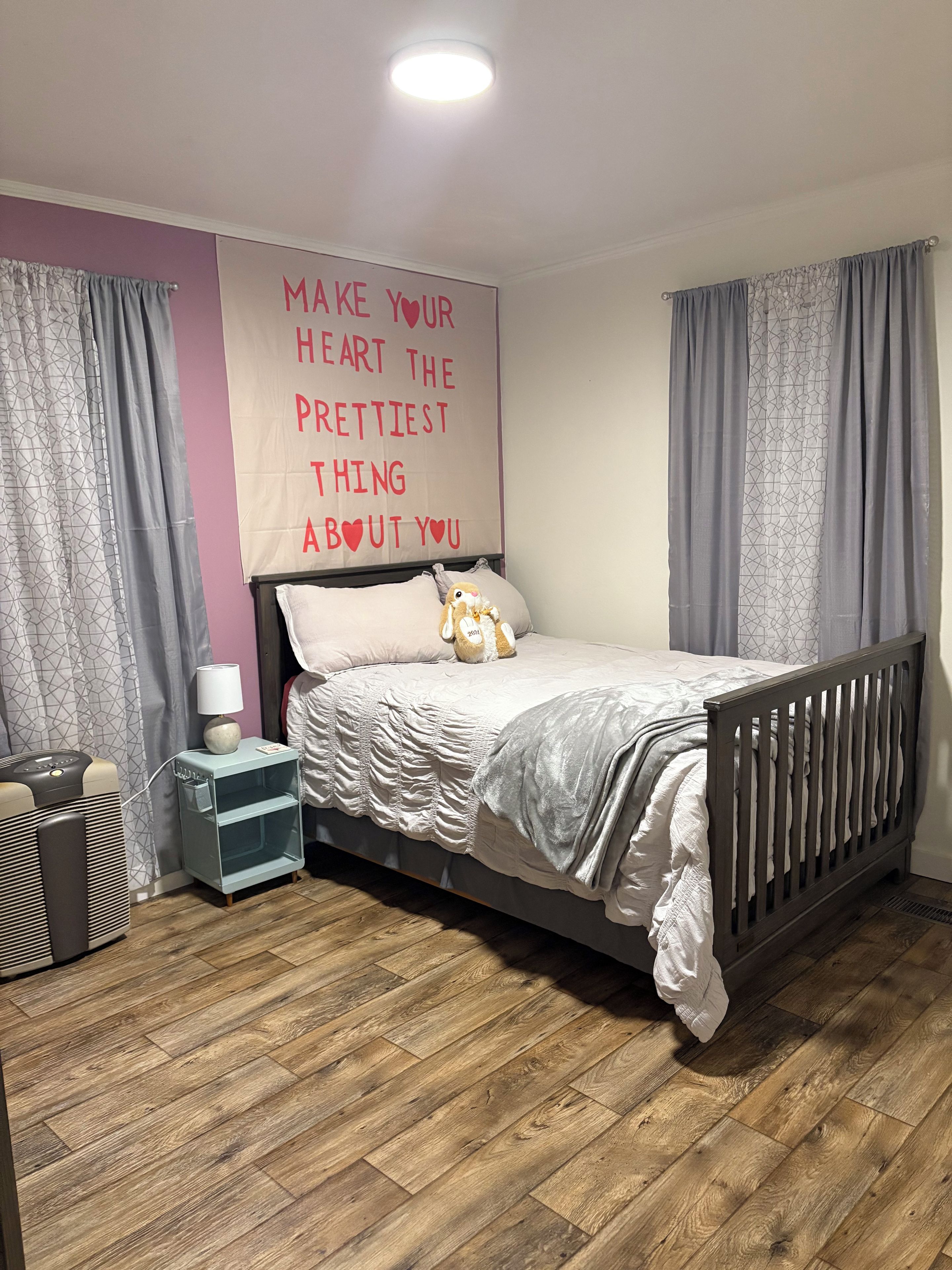 A bedroom with a bed, a bedside table, a wall decoration, and curtains.