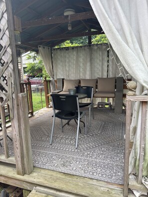 An outdoor seating area with a table and chairs, a patterned rug, and a wooden structure. - Little Linden Lodge: 2-bedroom house in charming McKenzie (McKenzie)